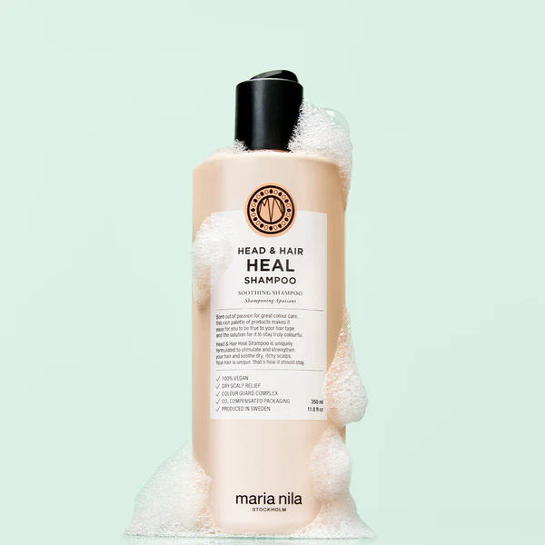 Flasche mit Maria Nila Head & Hair Heal Shampoo, umgeben von Schaum, auf mintgrünem Hintergrund.